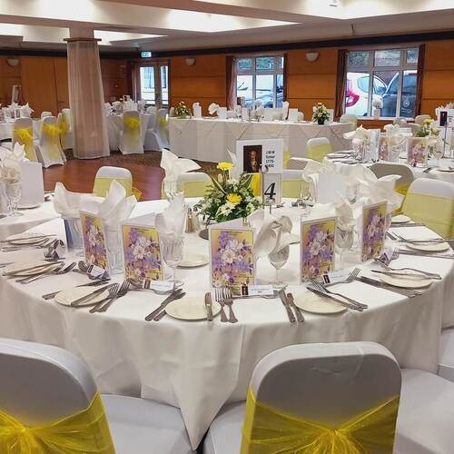 Hotel ballroom dressed for wedding with round tables, white linens, yellow chair sashes, floral centerpieces and dance floor