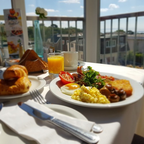 Sunlit balcony breakfast with fried and scrambled eggs, grilled tomato, hash brown, croissant, juice and coffee, sea view
