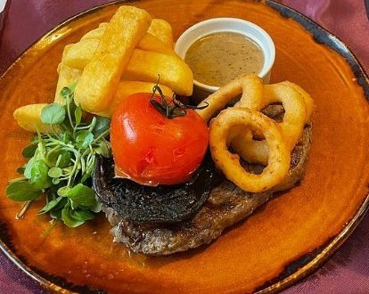 Grilled steak topped with black pudding and roasted tomato, served with onion rings, thick chips, peppercorn sauce and greens
