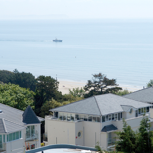 Coastal hotel villas with glass balconies overlooking sandy beach, treeline and calm sea with a boat on the horizon.