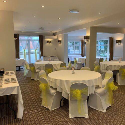 Private event room with round banquet tables covered in white linens, chairs wrapped with yellow organza bows, soft lighting.