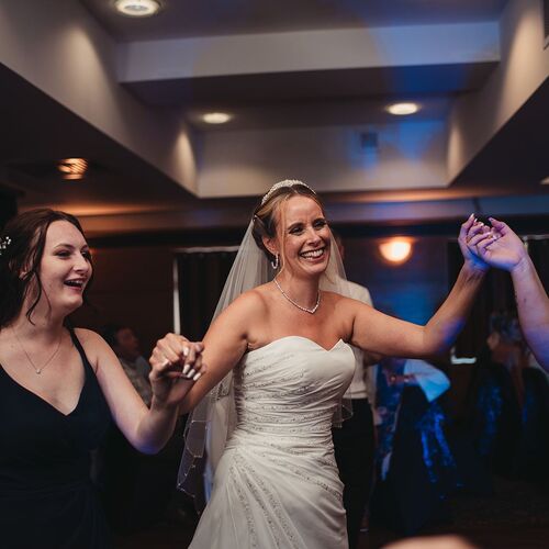 Bride in strapless gown and veil dancing with bridesmaids on a hotel ballroom floor, warm lighting and joyful reception atmosphere