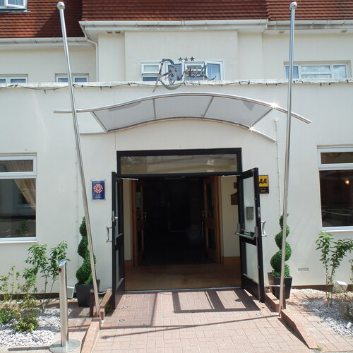 Hotel entrance with curved glass canopy and open double doors, potted spiral topiary, cream facade and AA rating plaque.