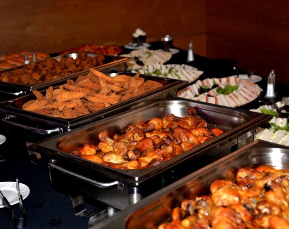 Hot buffet spread with roasted chicken drumsticks, breaded finger foods and assorted tea sandwiches in stainless chafing dishes.