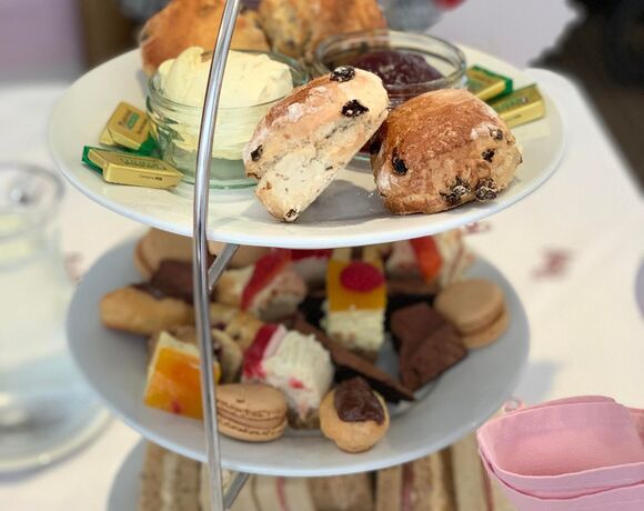 Three-tier afternoon tea stand with raisin scones, clotted cream, jam, assorted pastries, macarons and finger sandwiches.