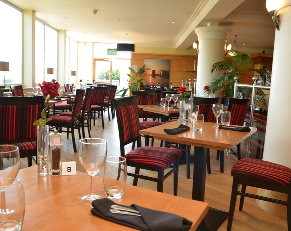 Sunlit hotel restaurant with wooden tables, red-striped chairs, single red roses and neatly set glassware