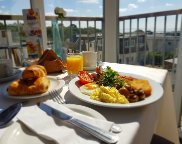 Sunlit balcony breakfast with fried and scrambled eggs, grilled tomato, hash brown, croissant, juice and coffee, sea view