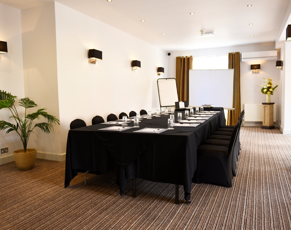 Small boardroom set for a meeting with black-draped tables, notepads and water glasses, flipchart and projector screen.