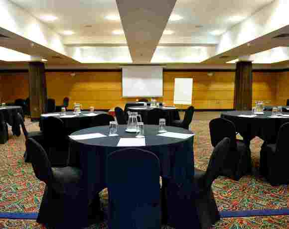 Hotel conference room set for a meeting: round tables with black linens, covered chairs, water pitchers and notepads.
