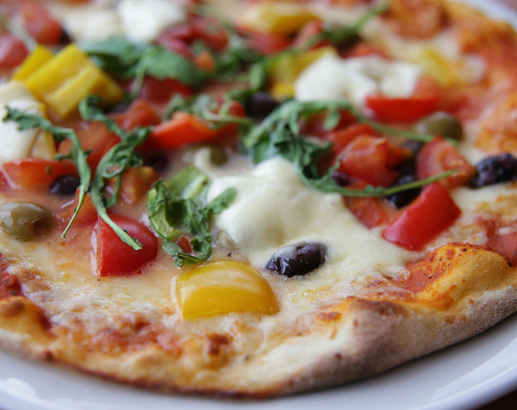 Thin-crust pizza with melted mozzarella, cherry tomatoes, yellow peppers, olives and arugula on a white plate