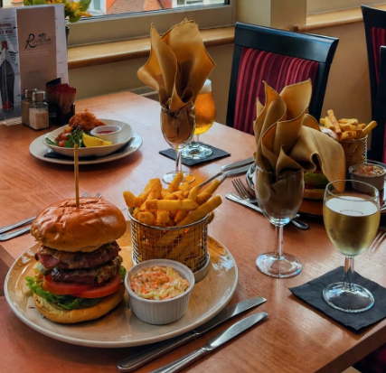 Gourmet double burger with lettuce, tomato and fries in a basket, coleslaw and beer and white wine on a cozy restaurant table.