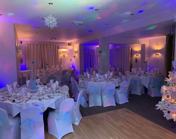 Winter banquet: round tables with white chair covers and bows, set tables, snowflake decor and blue-purple uplighting.