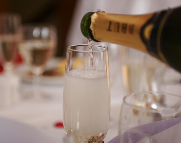 Champagne poured into a flute at an elegant white-tablecloth dining setting with sparkling glassware and a festive mood.