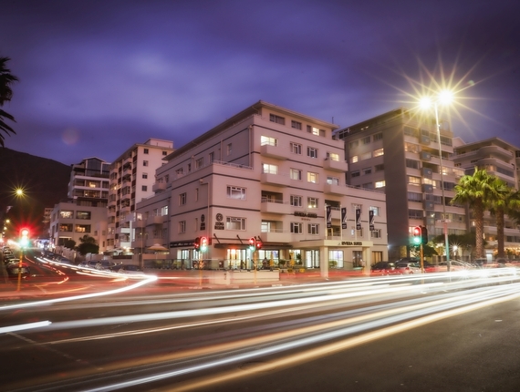 Riviera Suite with balconies and ground-floor café, beachfront street at dusk with palm trees and light trails