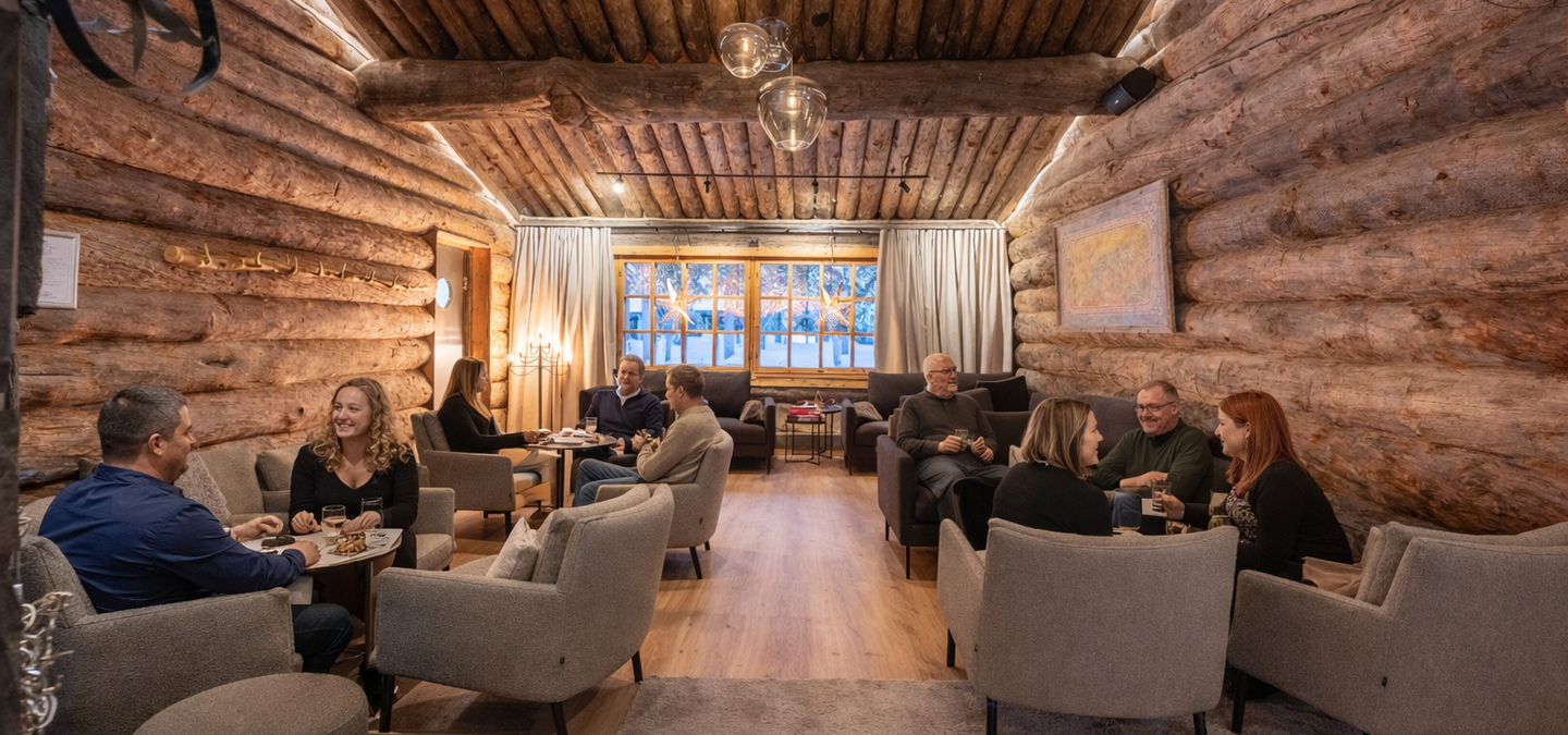 Cozy log cabin lounge with rustic wooden walls, warm lighting, and guests enjoying drinks and conversation around small tables