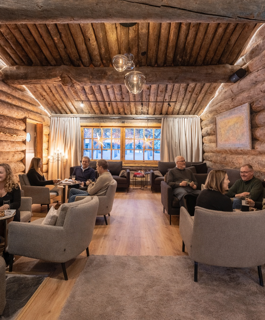 Cozy log cabin lounge with rustic wooden walls, warm lighting, and guests enjoying drinks and conversation around small tables