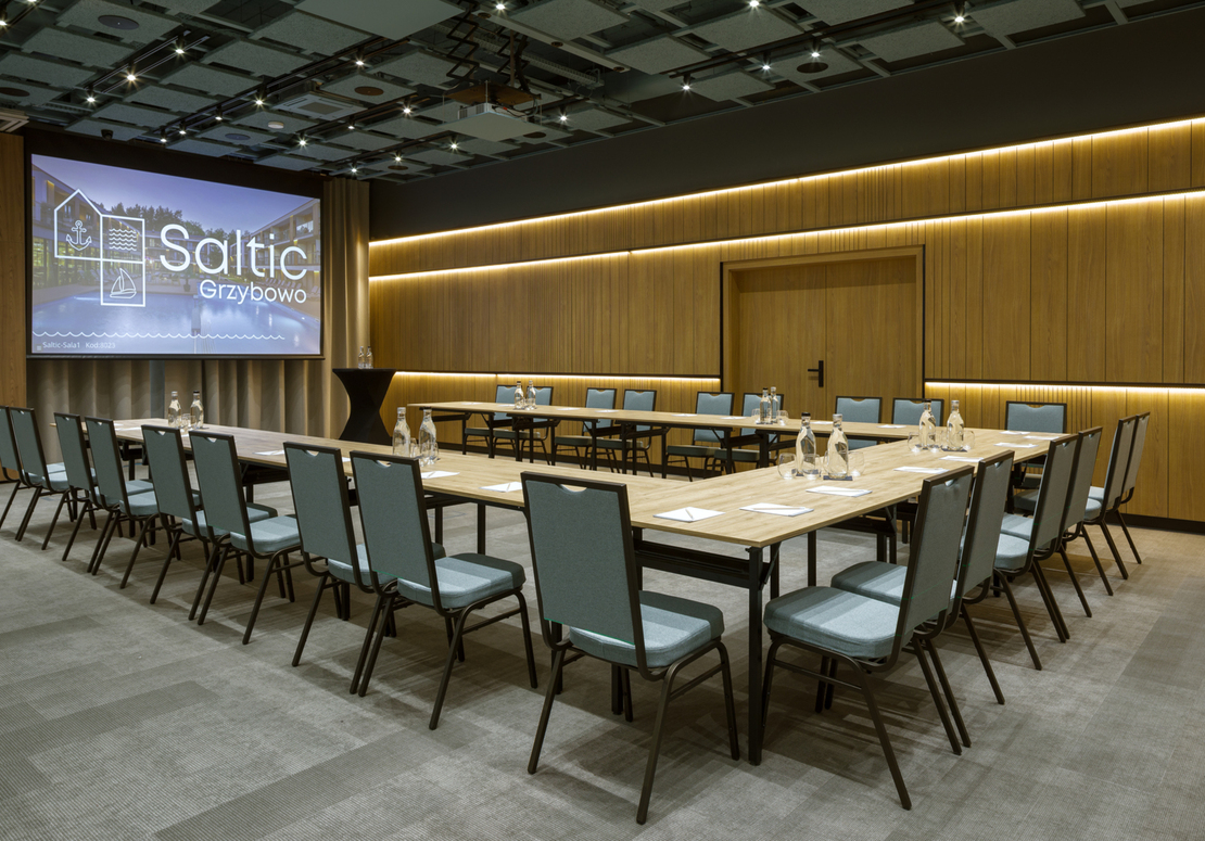 Konferenzraum in U-Form mit Leinwand 'Saltic Grzybowo', warmen Holzpaneelen und Wasserflaschen auf Tischen