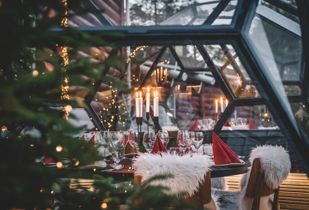 Katettu yksityisillallispöytä Three Elves -ravintolan lasi-iglussa, kynttilöitä, lampaantaljat tuoleilla ja joulukuusi