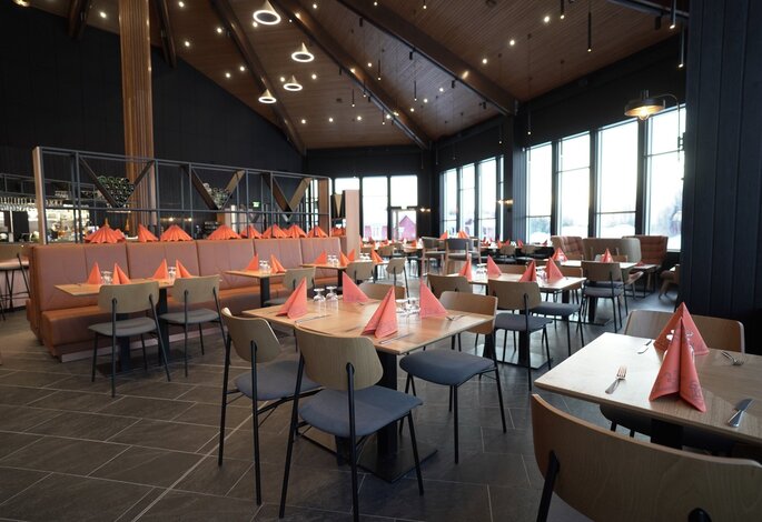 Santa’s Cuisine -ravintolan ruokailutila, jossa on riveittäin katettuja pöytiä, punaiset lautasliinat ja suuret ikkunat