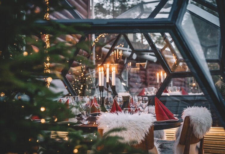Katettu yksityisillallispöytä Three Elves -ravintolan lasi-iglussa, kynttilöitä, lampaantaljat tuoleilla ja joulukuusi