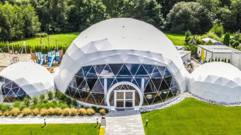 Geodesic dome hotel with glass-front central dome, circular entrance, linked smaller domes, lawn terrace and children's playground.