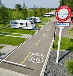Modern campsite with paved grassy caravan pitches, tree-lined road, entrance barrier and red Scandi Bikestation sign.