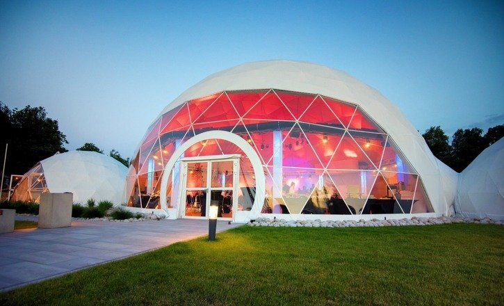 Szklana kopuła geodezyjna z łukowym wejściem, kolorowe oświetlenie wnętrza i goście wewnątrz, trawnik na przyjęcia plenerowe
