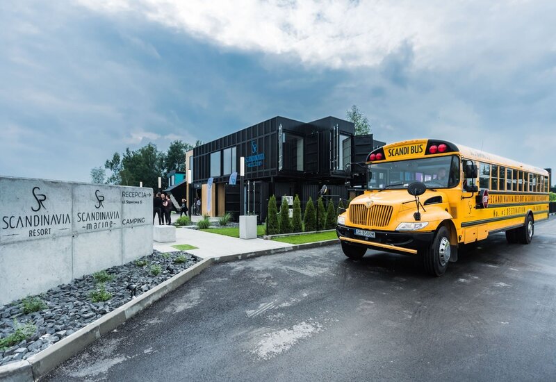 Nowoczesna czarna modułowa recepcja Scandinavia Resort, zadbane wejście i żółty autobus Scandi zaparkowany przy chodniku.