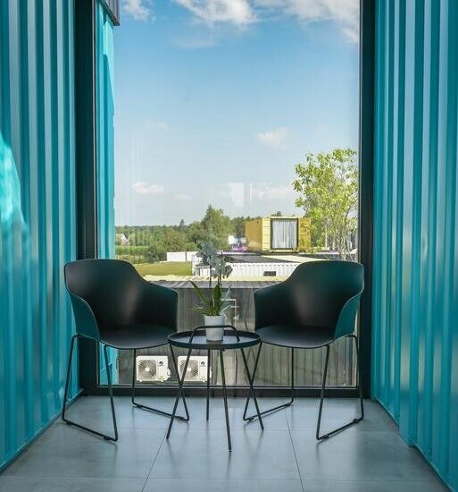 Dwa nowoczesne czarne fotele i stolik z rośliną przy panoramicznym oknie w turkusowym kontenerze, widok na wieś.