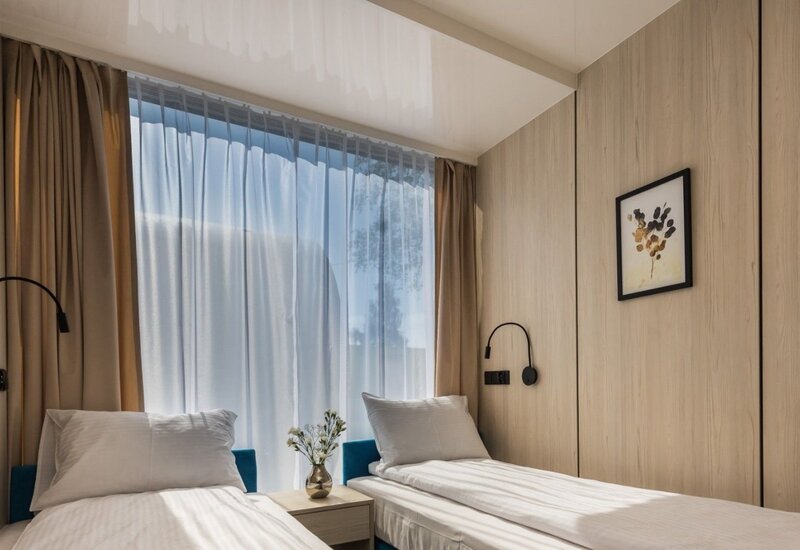 Nowoczesny pokój z drewnianymi panelami, dwiema pojedynczymi łóżkami, białą pościelą, stolikiem z wazonem, lampkami i naturalnym światłem