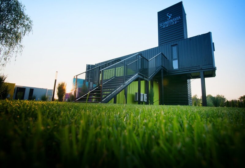 Nowoczesny hotel z kontenerów z metalowymi schodami, zielonym trawnikiem i tarasem oświetlonym zachodem słońca.