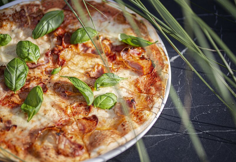 Pizza na cienkim cieście z roztopioną mozzarellą, złocistymi przypieczonymi brzegami i świeżą bazylią na białym talerzu.