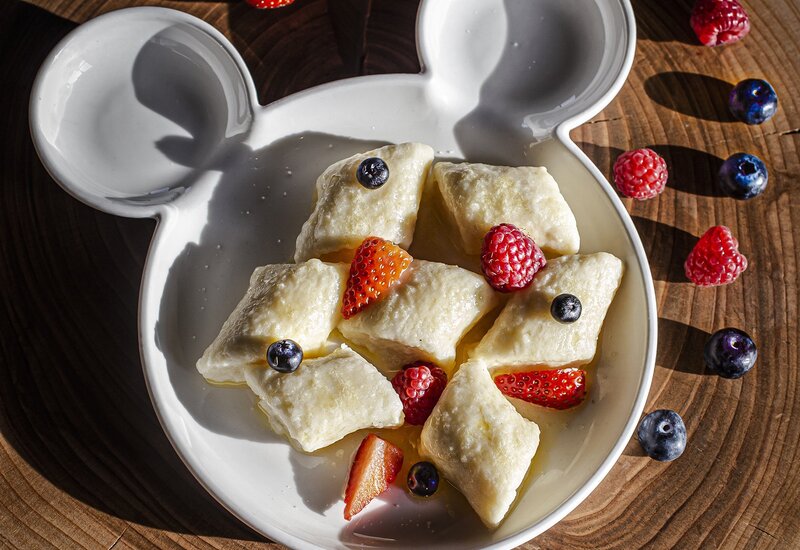 Ceramiczna miseczka w kształcie uszu z serowymi kluseczkami, miodem i świeżymi truskawkami, malinami i borówkami na drewnianej desce