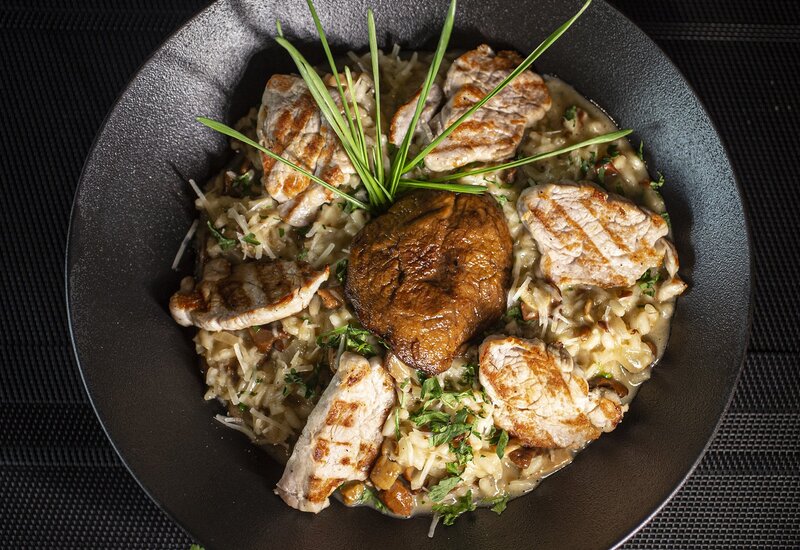 Kremowe risotto z grzybami podane z grillowanymi medalionami wieprzowiny i pieczonym portobello, ozdobione szczypiorkiem i natką pietruszki.