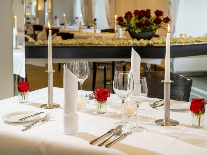 Romantisch gedeckter Restauranttisch mit weißen Leinen, brennenden Kerzen, roten Rosen, Weingläsern und feinem Besteck
