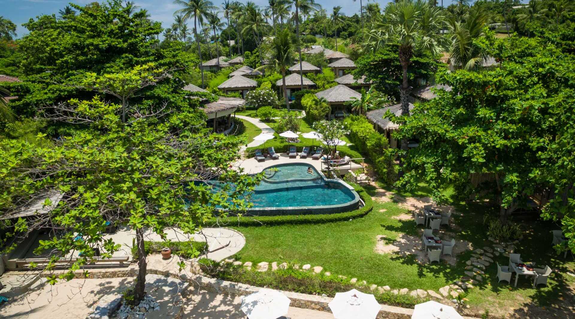 Tropical resort with private thatched-roof villas, central pool surrounded by loungers and umbrellas, lush greenery and outdoor dining areas