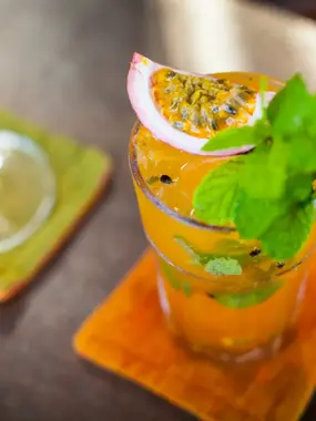Tropical passion fruit cocktail garnished with fresh mint leaves, served on a wooden table with a coaster nearby
