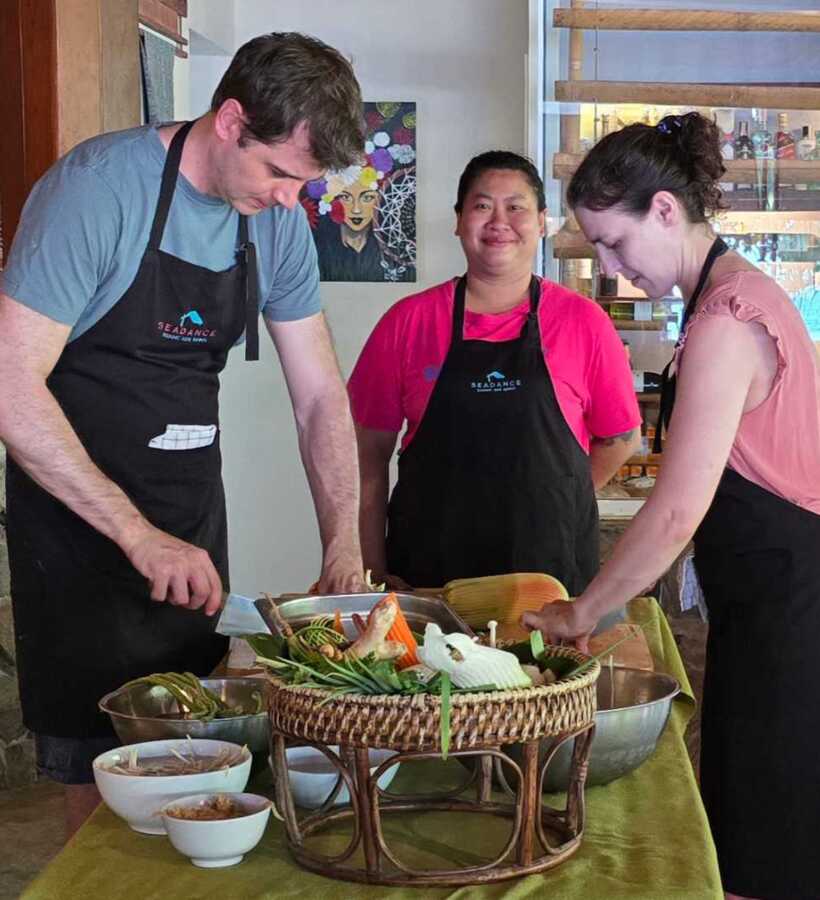 Three hotel guests in aprons preparing a traditional cooking class with fresh ingredients in a cozy, rustic dining area