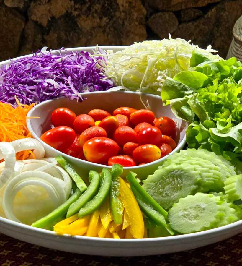 Fresh garden vegetable platter featuring cherry tomatoes, shredded carrot, purple cabbage, lettuce, sliced cucumber, bell peppers, and onion served on a white tray