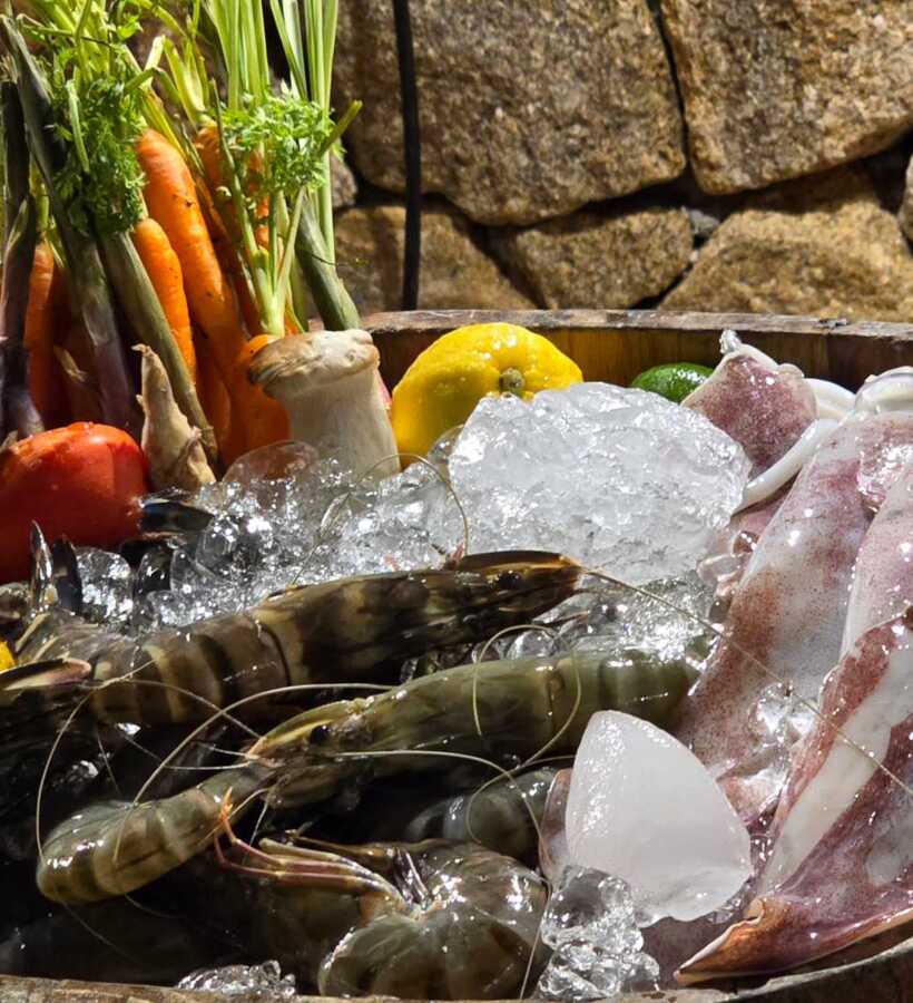 Fresh seafood and vibrant vegetables on ice in a rustic wooden barrel, highlighting a hotel’s farm-to-table dining experience