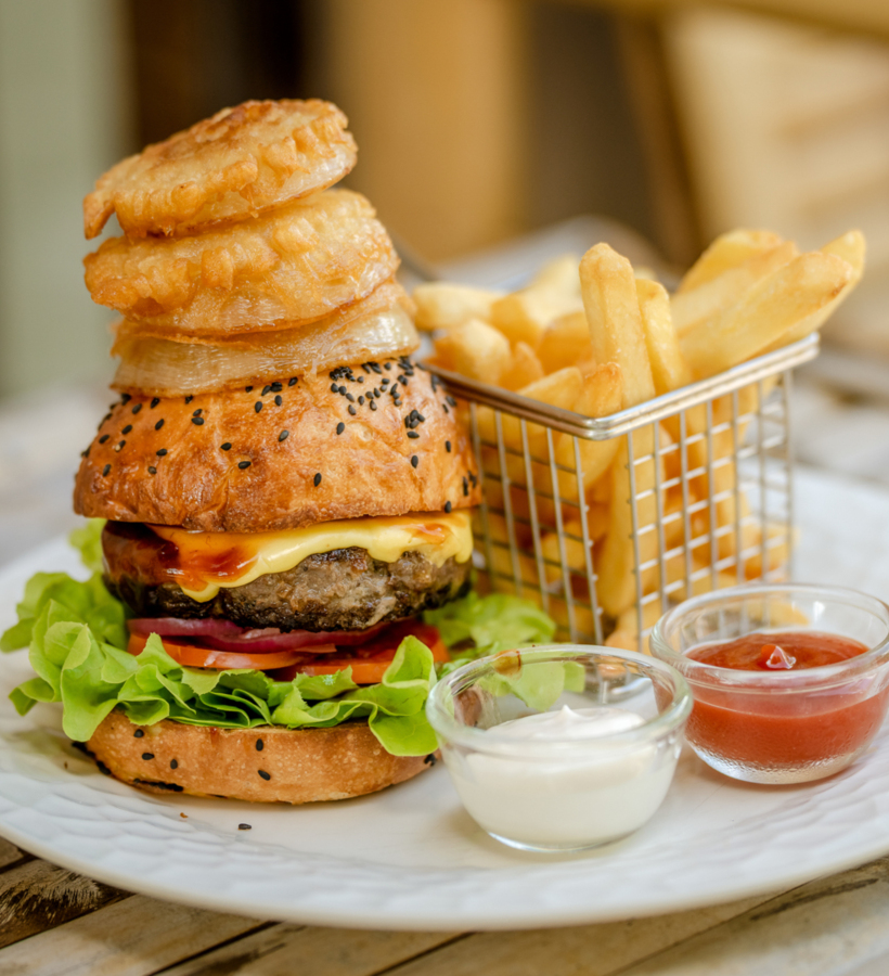 Gourmet cheeseburger with lettuce, tomato, and onion rings on a sesame bun, served with fries and dipping sauces