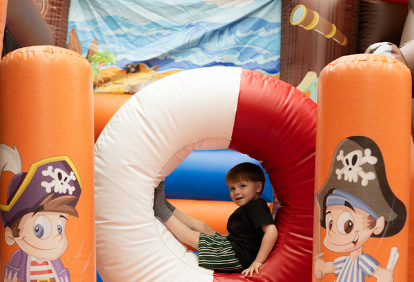Child in life-ring tunnel of pirate-themed inflatable bouncy castle, bright orange play area with cartoon pirate graphics