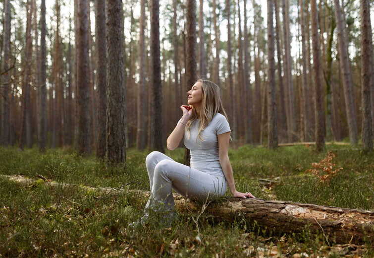Woman in gray activewear sits on a fallen log in a tranquil pine forest, enjoying the outdoors