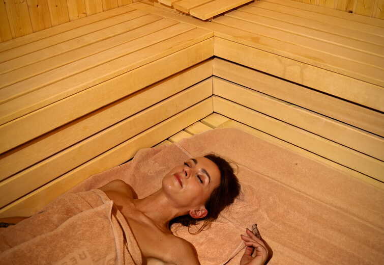 Guest relaxing on a towel in a wooden hotel sauna, reclining on a bench in a peaceful spa setting.