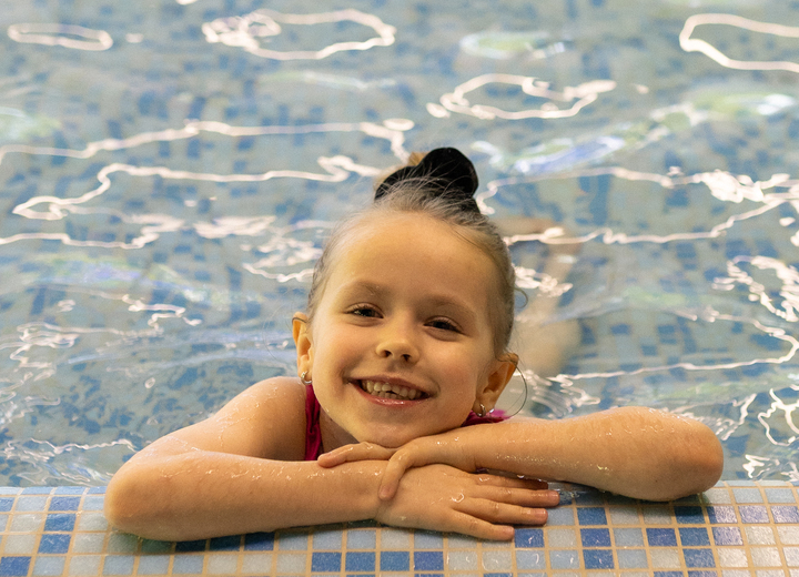 Smiling child resting on tiled edge of a hotel indoor pool, enjoying a family-friendly swimming area.