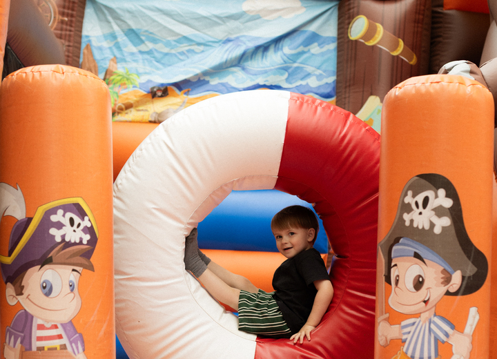 Child in life-ring tunnel of pirate-themed inflatable bouncy castle, bright orange play area with cartoon pirate graphics