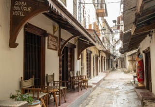 Shaba Boutique Hotel entrance with wooden chairs and tables along a narrow, historic stone-paved street lined with traditional buildings