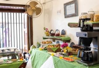 Breakfast buffet with pastries, fresh fruit, jams, cereals, coffee station, and colorful flower arrangements in a cozy dining area