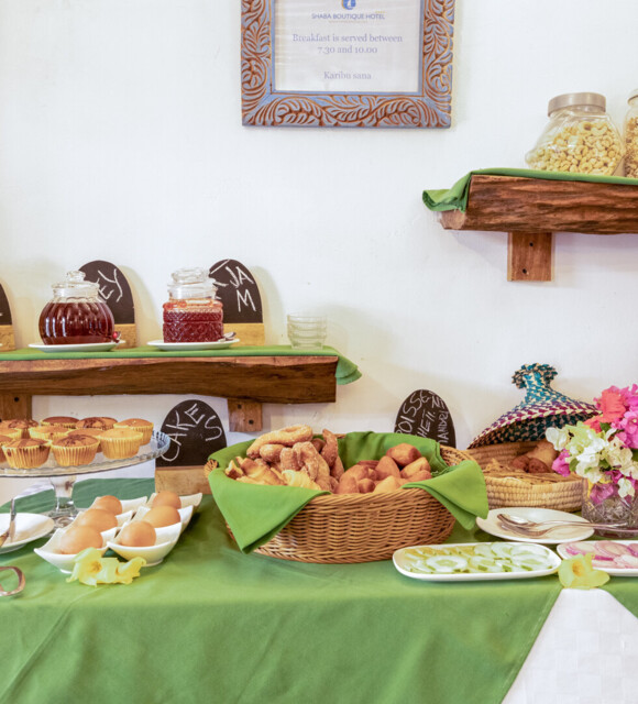 Breakfast buffet with fresh pastries, boiled eggs, sliced vegetables, jams, honey, cereals, and decorative flowers on a green tablecloth