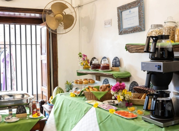 Breakfast buffet with pastries, fresh fruit, jams, cereals, coffee station, and colorful flower arrangements in a cozy dining area